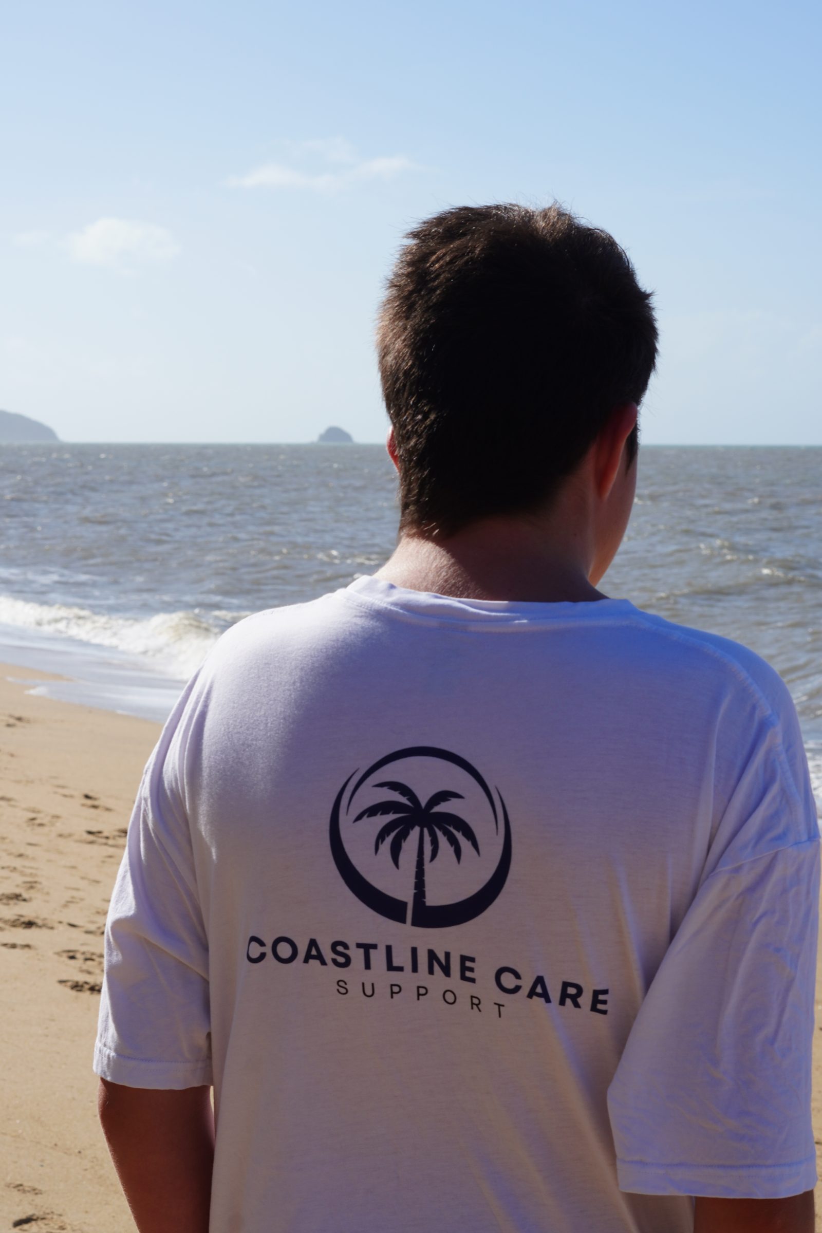 A Coastline Care support worker on a Cairns beach, the brand on his back
